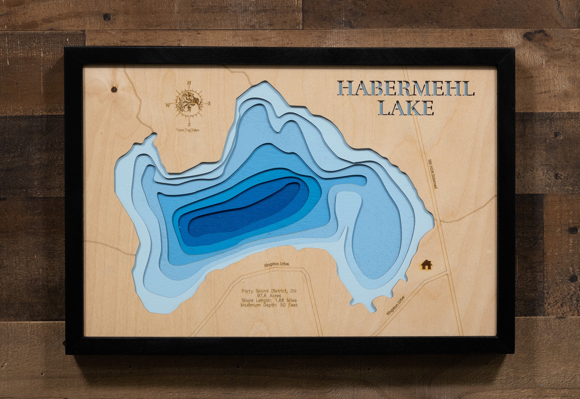 A highly detailed, laser-cut, and multi-layered wooden map of Habermehl Lake, a natural lake in the Parry Sound District of Ontario. The map shows the lake's distinct shape and its 1.68-mile shoreline. The varying depths of the lake, reaching a maximum of 50 feet, are represented by different layers of wood.