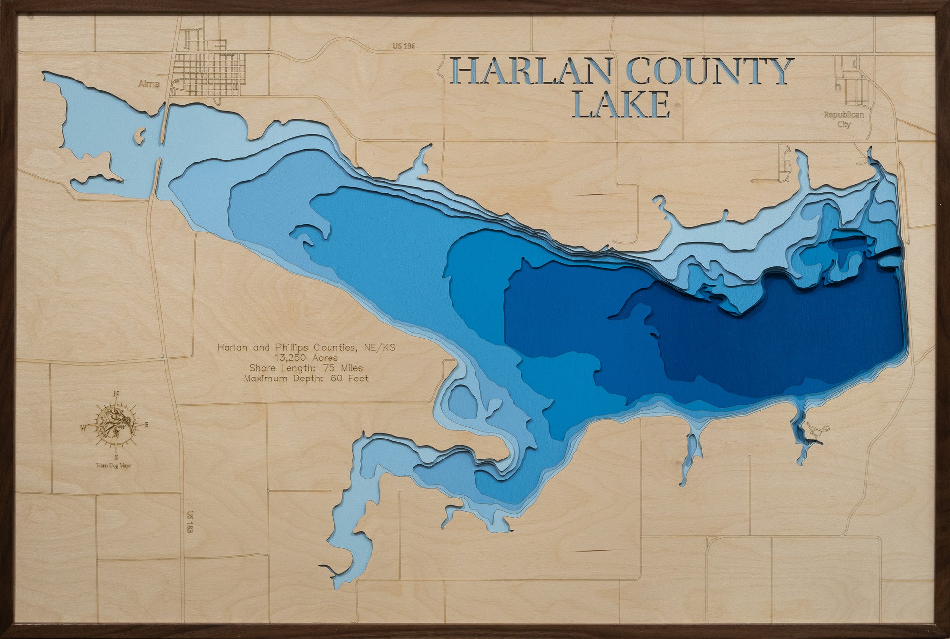 A laser-cut, layered wooden map of Harlan County Lake, located in Harlan County, Nebraska and Phillips County, Kansas. The shape of the reservoir, spanning across the state line, is clearly visible within the south-central landscape. The varying depths of the lake, reaching a maximum of 95 feet, are represented by different layers of wood, creating a three-dimensional effect of this important bi-state water body.