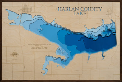 A laser-cut, layered wooden map of Harlan County Lake, located in Harlan County, Nebraska and Phillips County, Kansas. The shape of the reservoir, spanning across the state line, is clearly visible within the south-central landscape. The varying depths of the lake, reaching a maximum of 95 feet, are represented by different layers of wood, creating a three-dimensional effect of this important bi-state water body.