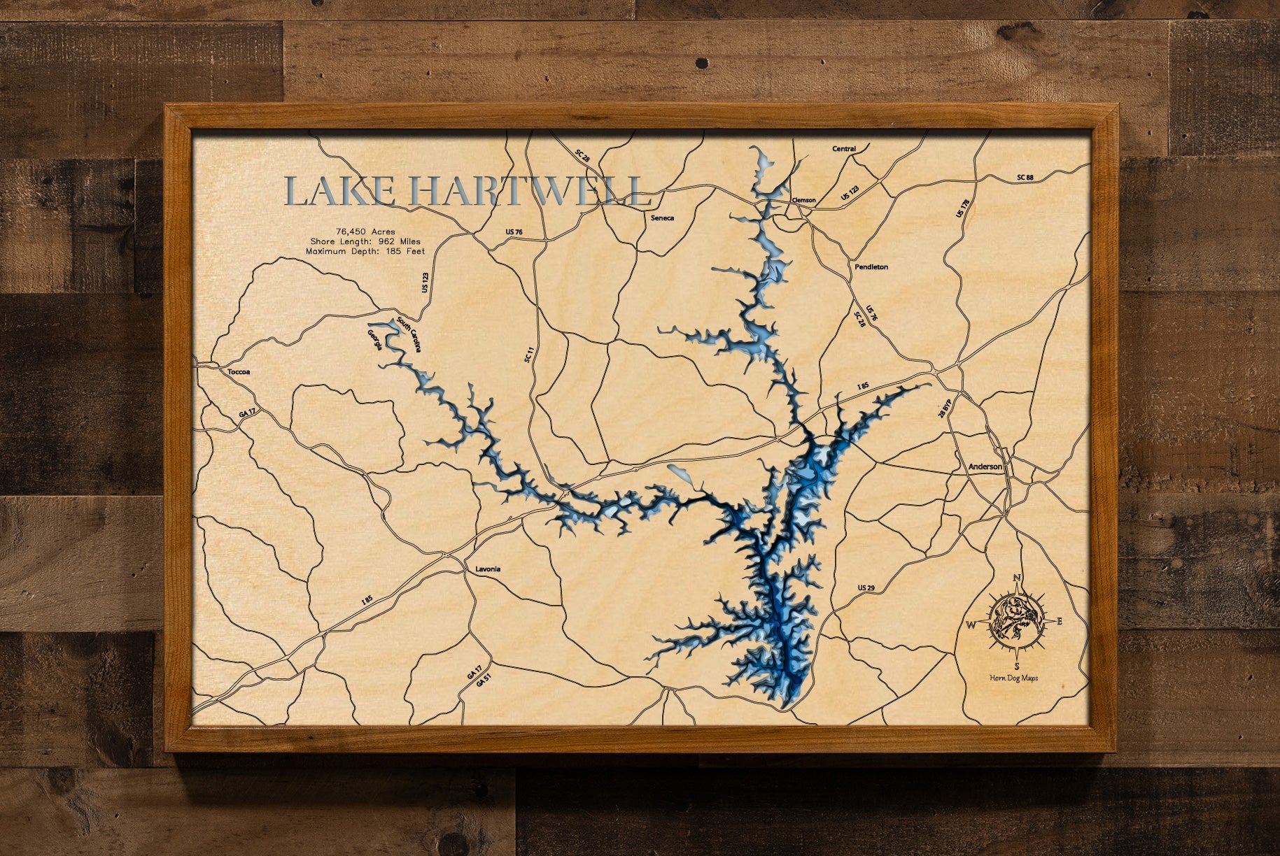 A highly detailed, laser-cut, and multi-layered wooden map of Lake Hartwell, a large reservoir that spans the borders of South Carolina and Georgia. The map shows the lake's distinct shape and its extensive 962-mile shoreline. The varying depths of the lake, reaching a maximum of 185 feet, are represented by different layers of wood.