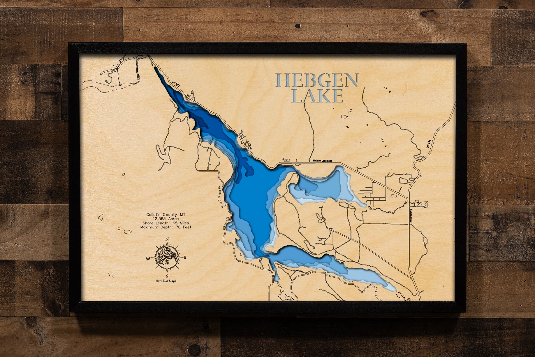 A highly detailed, laser-cut, and multi-layered wooden map of Hebgen Lake, a large reservoir in Gallatin County, Montana. The map shows the lake's distinct shape and its extensive 65-mile shoreline. The varying depths of the lake, reaching a maximum of 70 feet, are represented by different layers of wood, illustrating its impressive underwater topography.