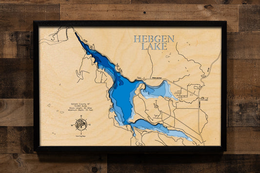 A highly detailed, laser-cut, and multi-layered wooden map of Hebgen Lake, a large reservoir in Gallatin County, Montana. The map shows the lake's distinct shape and its extensive 65-mile shoreline. The varying depths of the lake, reaching a maximum of 70 feet, are represented by different layers of wood, illustrating its impressive underwater topography.