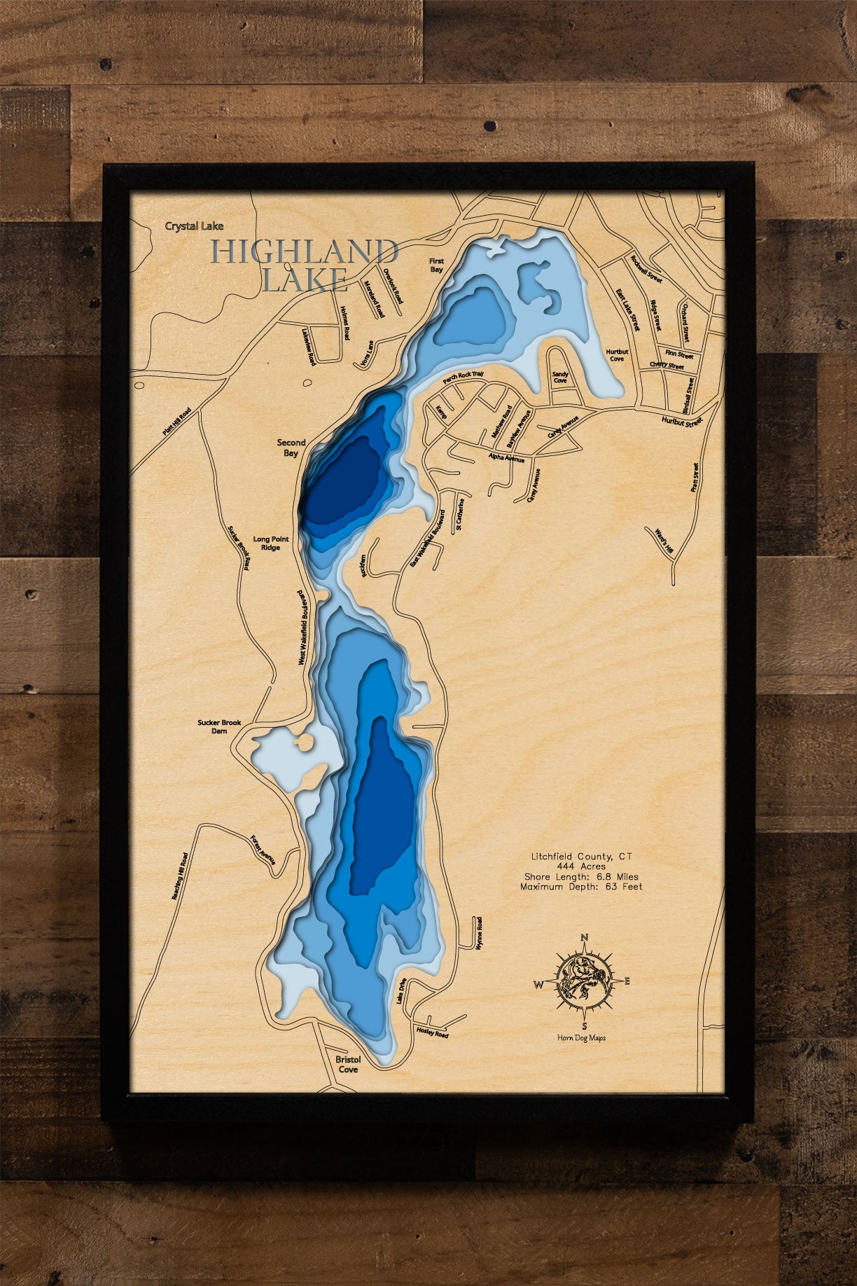 A laser-cut, layered wooden map of Highland Lake in Litchfield County, Connecticut. The distinct shape of this natural lake, with its 6.8-mile shoreline, is clearly visible within the forested landscape of Winchester. The varying depths of the lake, reaching a maximum of 110 feet, are represented by different layers of wood, illustrating its impressive underwater topography.
