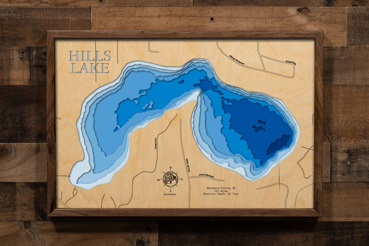 A precision laser-cut, multi-layered wooden map of Hills Lake in Waushara County, Wisconsin, a 125-acre Central Sands lake with a clean sandy bottom and moderately clear water near Wild Rose and Wautoma. The natural wood top layer captures the lake's natural shoreline in fine detail, while a light-to-dark blue gradient conveys its 22-foot depth. A handcrafted statement piece for any Wisconsin lake cabin, home, or outdoor enthusiast's wall.