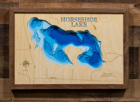 A framed wooden topographic map of Horseshoe Lake, featuring layered blue and light blue wood cutouts representing the lake's depth, mounted on a rustic dark wood wall.