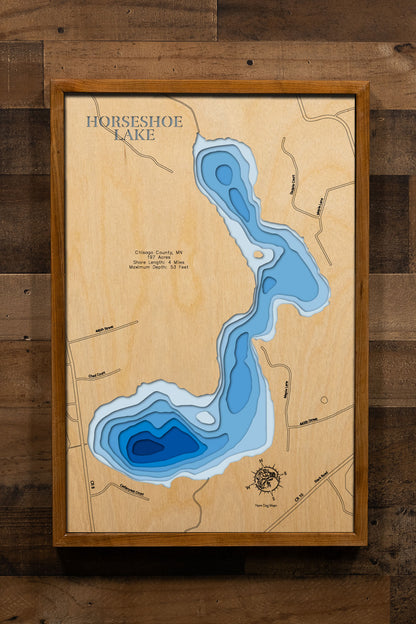 A precision laser-cut, multi-layered wooden map of Horseshoe Lake in Chisago County, Minnesota, a 197-acre lake named for its distinctive horseshoe-shaped shoreline near Harris and North Branch. The natural wood top layer captures 4 miles of shoreline in fine detail, while a light-to-dark blue gradient conveys the lake's 53-foot depth. A handcrafted statement piece for any Minnesota lake home, cabin, or outdoor enthusiast's wall.