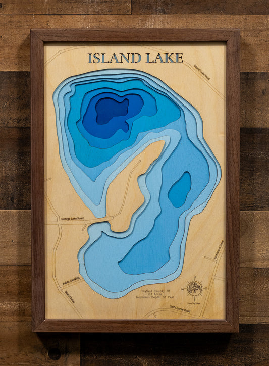 A precision laser-cut, multi-layered wooden map of Island Lake in Bayfield County, Wisconsin. The natural wood top layer captures the lake's intimate shoreline in fine detail, while a light-to-dark blue gradient highlights the water's depth and dimension. A distinctive, rustic statement piece crafted for cabin walls, fishing lodges, or any Wisconsin Northwoods-inspired living space.