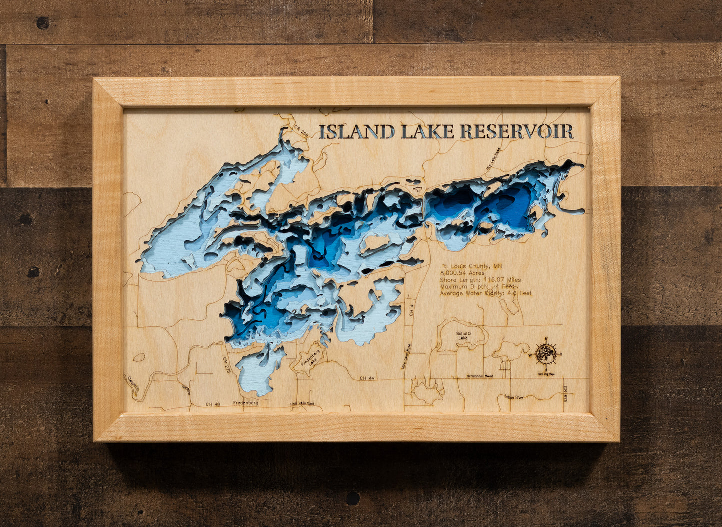 A laser-cut, layered wooden map of Island Lake Reservoir in St. Louis County, Minnesota. The distinct shape of this large reservoir, with its 116.07-mile shoreline and numerous islands, is clearly visible within the forested landscape of northern Minnesota. The varying depths of the reservoir, reaching a maximum of 94 feet, are represented by different layers of wood, illustrating its impressive underwater topography.