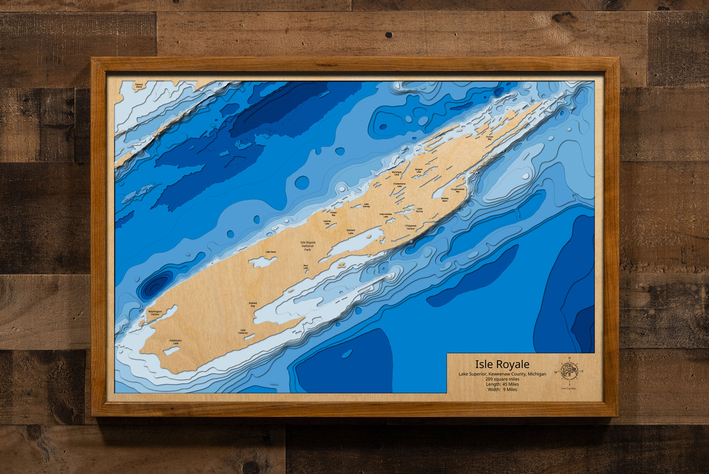 A laser-cut, layered wooden map showcasing Isle Royale, detailed with its intricate network of inland lakes, rugged topography, and surrounding smaller islands, all set within the vast expanse of Lake Superior. The map highlights the island's elongated shape and its remote location, emphasizing its wilderness character as a national park.