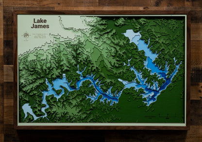A laser-cut, layered wooden map of Lake James in North Carolina. The distinct shape of this large reservoir, with its numerous arms and 150-mile shoreline, is clearly visible as it spans Burke and McDowell Counties. The varying depths of the lake, reaching a maximum of 120 feet, are represented by different layers of wood, illustrating its impressive underwater topography.