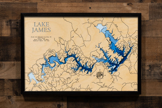 A laser-cut, layered wooden map of Lake James in North Carolina. The distinct shape of this large reservoir, with its numerous arms and 150-mile shoreline, is clearly visible as it spans Burke and McDowell Counties. The varying depths of the lake, reaching a maximum of 120 feet, are represented by different layers of wood, illustrating its impressive underwater topography.