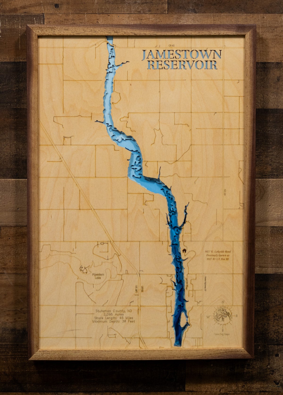 A highly detailed, laser-cut, and multi-layered wooden map of Jamestown Reservoir in Stutsman County, North Dakota. The map highlights the 2,095-acre reservoir's winding 8-mile length along the James River valley, with depth contours showing the 38-foot maximum depth, the unique peninsula and island features, and the intricate 45 miles of shoreline.