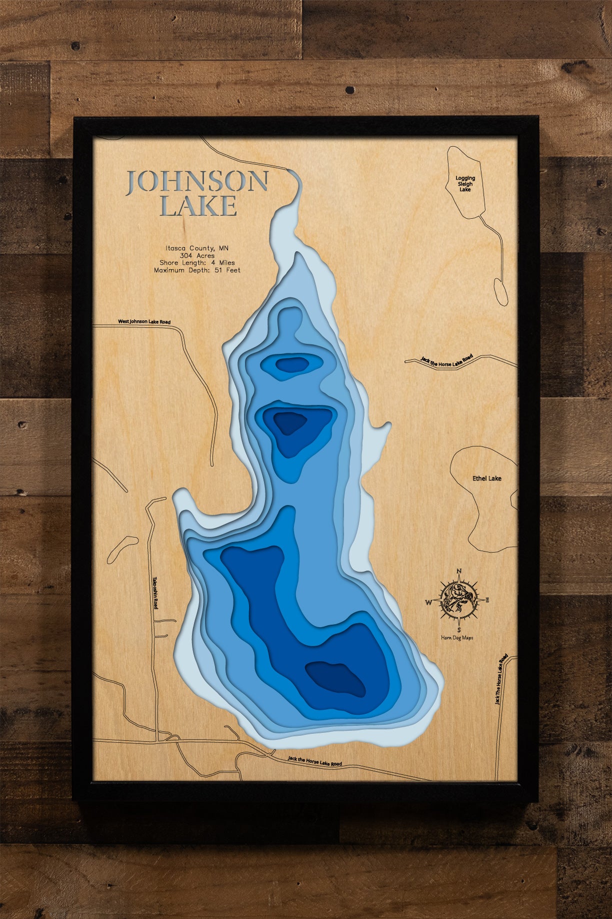 A precision laser-cut, multi-layered wooden map of Johnson Lake in Itasca County, Minnesota — a clear water Northwoods lake two miles north of Marcell. The natural wood top layer captures 4 miles of forested shoreline in fine detail, while a light-to-dark blue gradient conveys the lake's 51-foot depth. A handcrafted statement piece for any Minnesota cabin, lake home, or Northwoods enthusiast's wall.