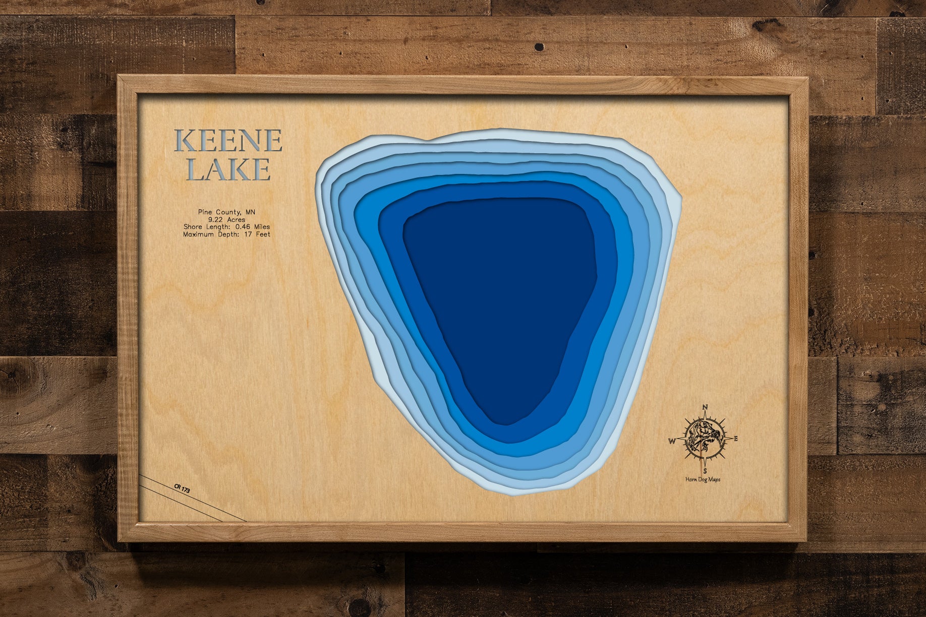 A detailed, laser-cut, multi-layered wooden map of Keene Lake in Pine County, Minnesota, showcasing the intimate 9.22-acre lake with half a mile of natural shoreline near Hinckley. The topographic design features natural wood layers highlighting the surrounding pine forest landscape and graduated blue water layers illustrating depths to the 17-foot maximum.
