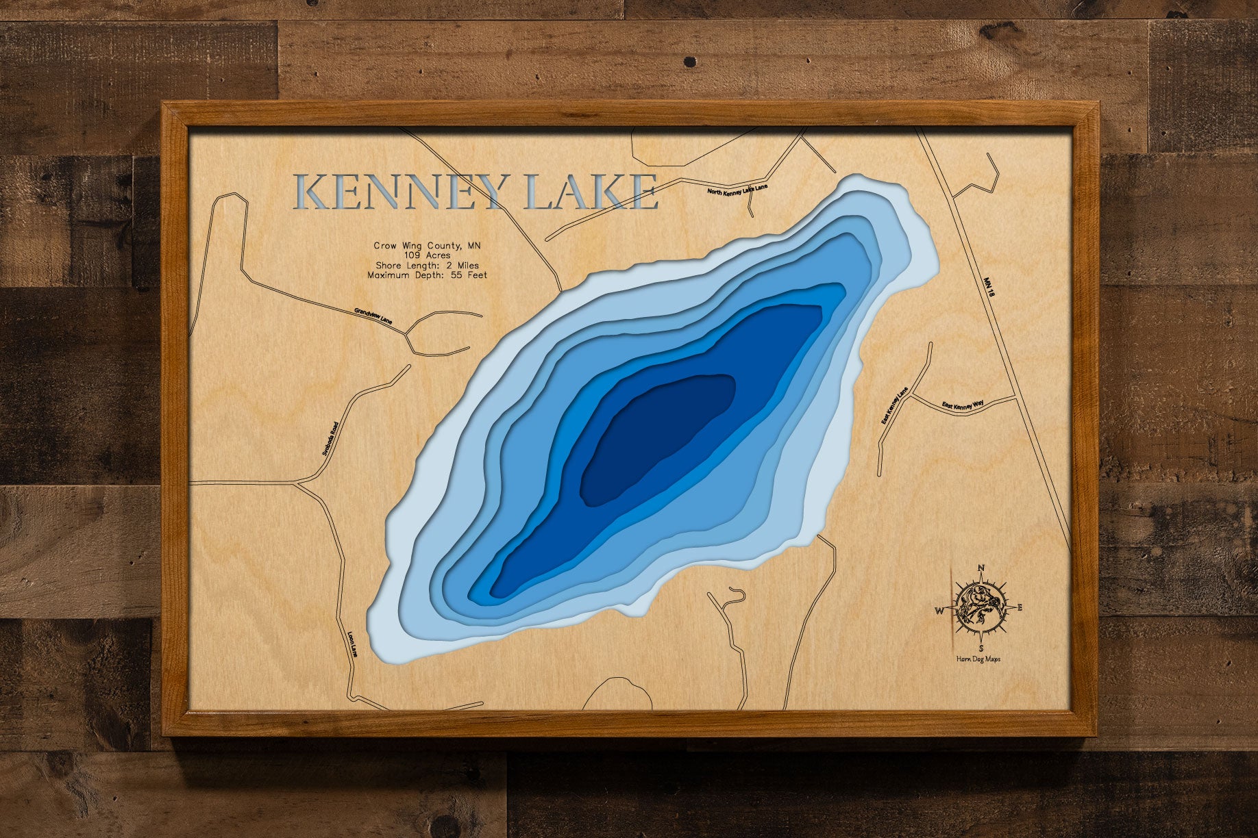 A precision laser-cut, multi-layered wooden map of Kenney Lake in Crow Wing County, Minnesota, near Garrison on the western edge of the Mille Lacs area. The natural wood top layer captures 2 miles of shoreline in fine detail, while a light-to-dark blue gradient conveys the lake's impressive 55-foot depth. A handcrafted statement piece for any Minnesota lake cabin, home, or outdoor enthusiast's wall.