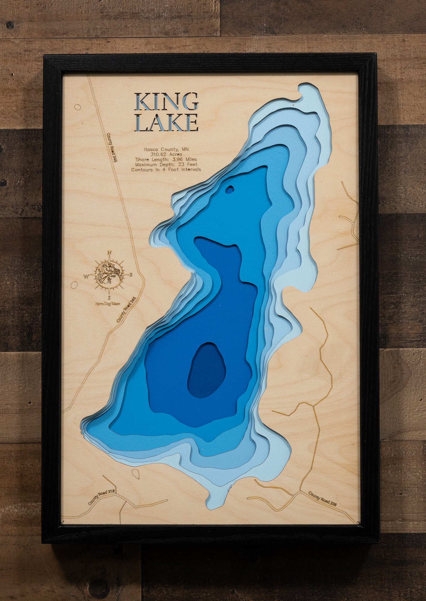 A laser-cut, layered wooden map of King Lake in Itasca County, Minnesota. The distinct shape of this natural lake, with its 3.96-mile shoreline, is clearly visible within the forested landscape of northern Minnesota. The varying depths of the lake, reaching a maximum of 23 feet, are represented by different layers of wood, illustrating its impressive underwater topography.
