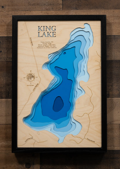 A laser-cut, layered wooden map of King Lake in Itasca County, Minnesota. The distinct shape of this natural lake, with its 3.96-mile shoreline, is clearly visible within the forested landscape of northern Minnesota. The varying depths of the lake, reaching a maximum of 23 feet, are represented by different layers of wood, illustrating its impressive underwater topography.