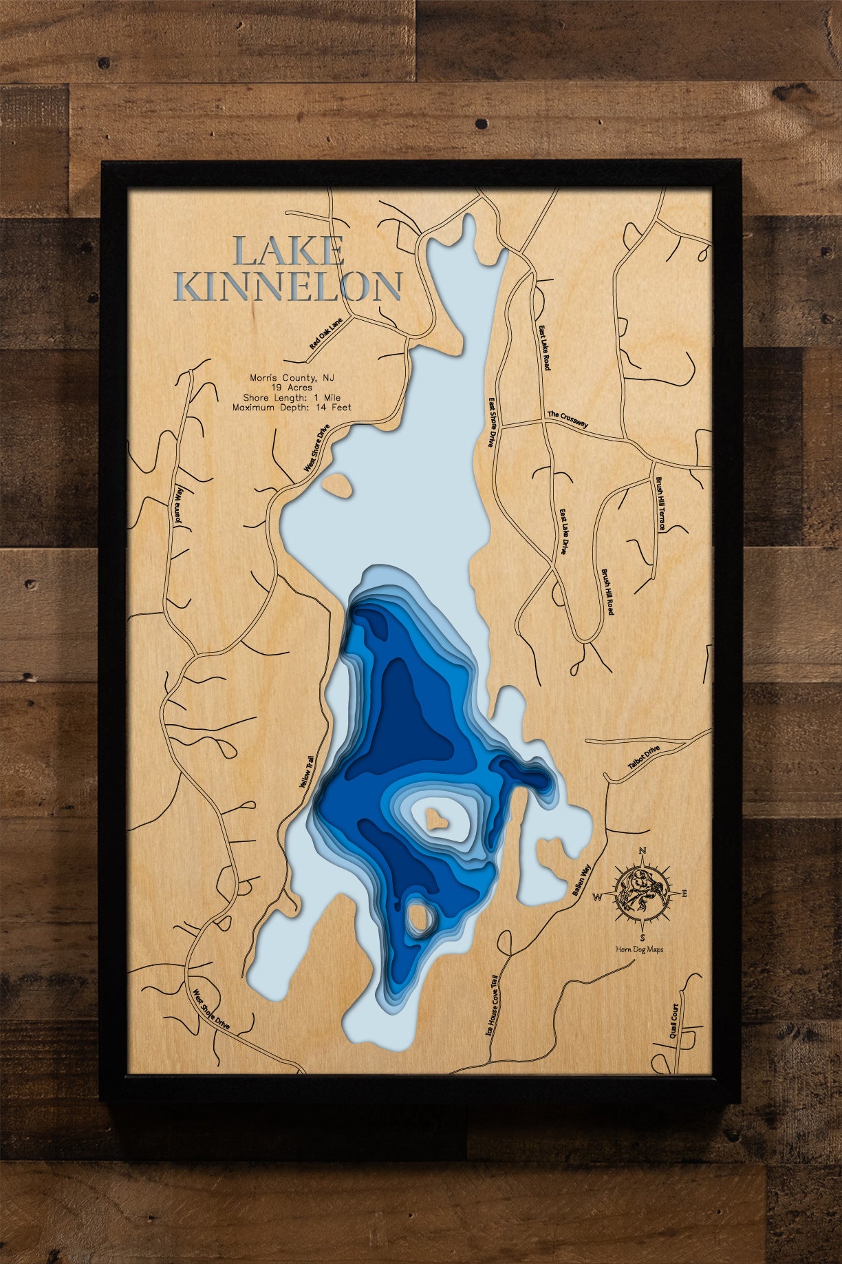 A beautifully detailed, laser-cut, multi-layered wooden topographical map of Lake Kinnelon in Morris County, New Jersey, showcasing the intimate 19-acre private lake within the Smoke Rise community featuring the historic chapel island, depth contours from the 6-foot average to the 14-foot maximum in Talbot Cove, and the distinctive underwater tree stumps. The natural wood top layer frames approximately one mile of shoreline, while graduated blue layers create an elegant visual depth gradient.