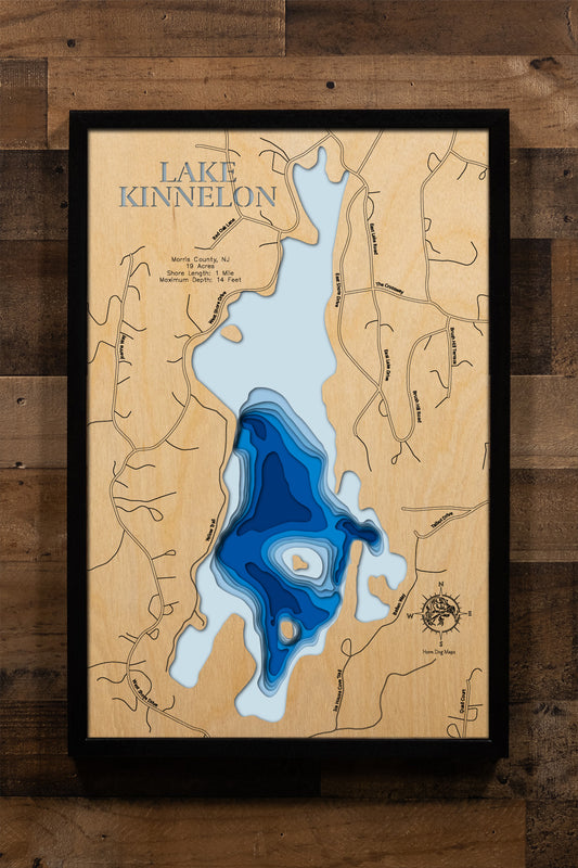 A beautifully detailed, laser-cut, multi-layered wooden topographical map of Lake Kinnelon in Morris County, New Jersey, showcasing the intimate 19-acre private lake within the Smoke Rise community featuring the historic chapel island, depth contours from the 6-foot average to the 14-foot maximum in Talbot Cove, and the distinctive underwater tree stumps. The natural wood top layer frames approximately one mile of shoreline, while graduated blue layers create an elegant visual depth gradient.