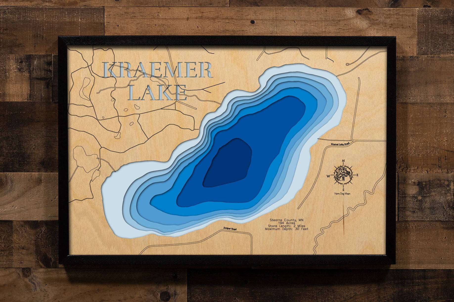 A precision laser-cut, multi-layered wooden map of Kraemer Lake in Stearns County, Minnesota, located two miles southwest of St. Joseph near St. Cloud. The natural wood top layer captures 2 miles of shoreline in fine detail, while a light-to-dark blue gradient conveys the lake's 30-foot depth. A handcrafted statement piece for any Minnesota lake home, cabin, or outdoor enthusiast's wall.