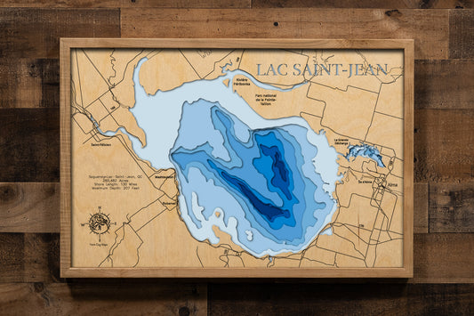 A magnificently detailed, laser-cut, multi-layered wooden topographical map of Lac Saint-Jean in Saguenay–Lac-Saint-Jean, Quebec, showcasing the expansive 260,482-acre inland sea measuring 45 by 34 kilometers with 130 miles of shoreline featuring picturesque villages and 42 kilometers of sandy beaches. The natural wood top layer frames the mouths of major rivers and the Véloroute des Bleuets route, while graduated blue layers create a stunning visual gradient from shallow waters to the 207-foot maximum dept