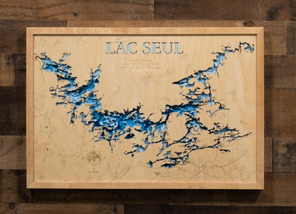 A laser-cut, layered wooden map of Lac Seul in Kenora District, Ontario, Canada. The distinct, crescent-shaped outline of this massive reservoir, with its 3,000-mile shoreline and countless islands, is clearly visible within the forested landscape of northwestern Ontario. The varying depths of the lake, reaching a remarkable maximum of 155 feet, are represented by different layers of wood, illustrating its impressive underwater topography.