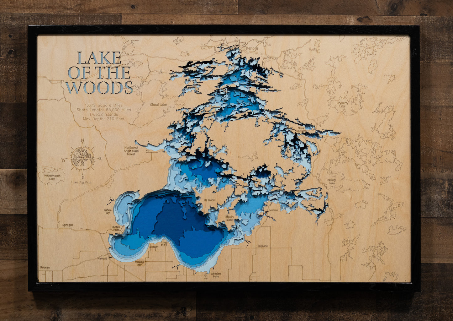A highly detailed, laser-cut, and multi-layered wooden map of the Minnesota portion of Lake of the Woods, a natural lake in Lake of the Woods and Roseau Counties. The map shows the lake's distinct shape, its massive size, and its 1,000+ miles of shoreline, as well as the unique Northwest Angle. The varying depths of the lake, reaching a maximum of 110 feet, are represented by different layers of wood.