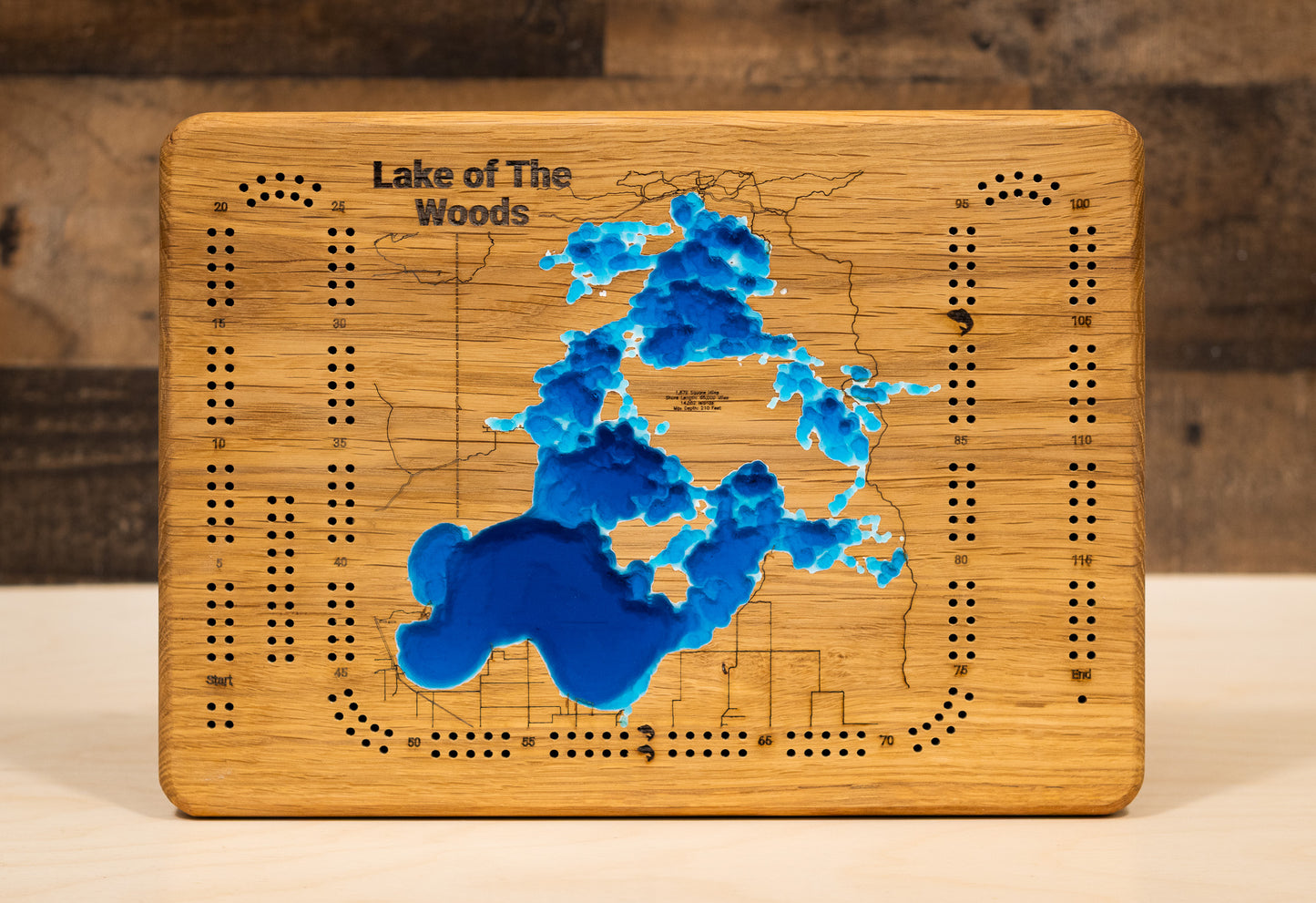 A highly detailed, laser-cut, and multi-layered wooden map of the Minnesota portion of Lake of the Woods, a natural lake in Lake of the Woods and Roseau Counties. The map shows the lake's distinct shape, its massive size, and its 1,000+ miles of shoreline, as well as the unique Northwest Angle. The varying depths of the lake, reaching a maximum of 110 feet, are represented by different layers of wood.