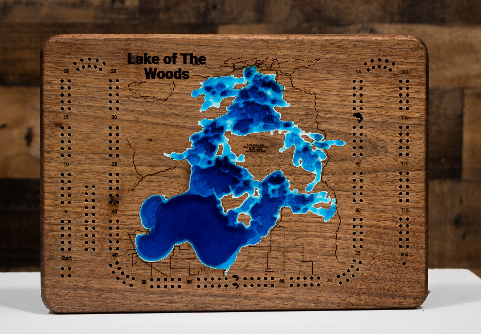 A highly detailed, laser-cut, and multi-layered wooden map of the Minnesota portion of Lake of the Woods, a natural lake in Lake of the Woods and Roseau Counties. The map shows the lake's distinct shape, its massive size, and its 1,000+ miles of shoreline, as well as the unique Northwest Angle. The varying depths of the lake, reaching a maximum of 110 feet, are represented by different layers of wood.