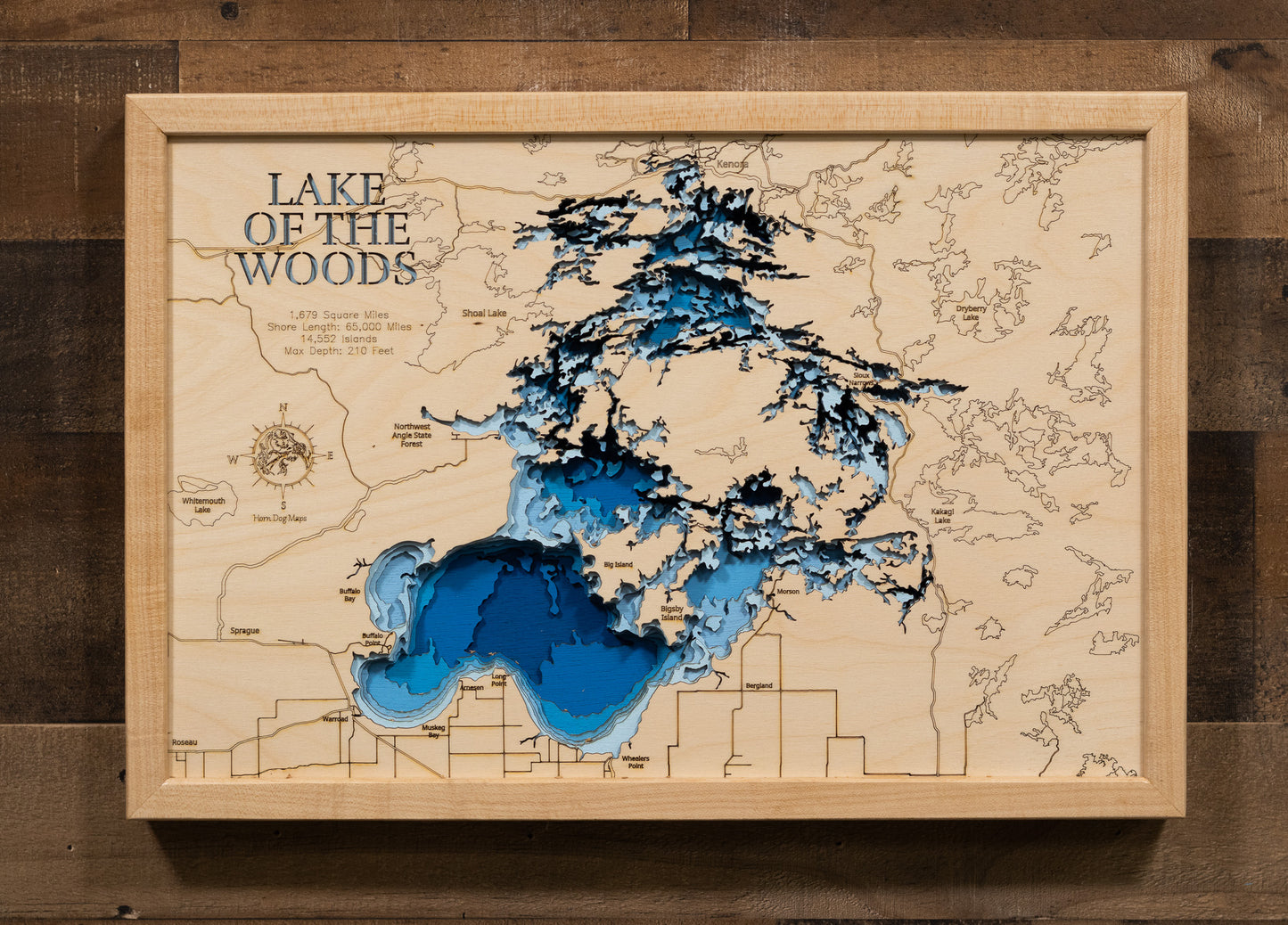 A highly detailed, laser-cut, and multi-layered wooden map of the Minnesota portion of Lake of the Woods, a natural lake in Lake of the Woods and Roseau Counties. The map shows the lake's distinct shape, its massive size, and its 1,000+ miles of shoreline, as well as the unique Northwest Angle. The varying depths of the lake, reaching a maximum of 110 feet, are represented by different layers of wood.