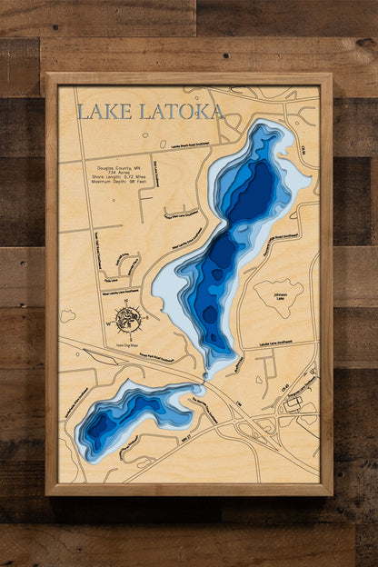 A laser-cut, layered wooden map of Lake Latoka in Douglas County, Minnesota. The distinct shape of this natural lake, with its 5.72-mile shoreline, is clearly visible within the landscape of west-central Minnesota. The varying depths of the lake, reaching a maximum of 98 feet, are represented by different layers of wood, illustrating its impressive underwater topography.