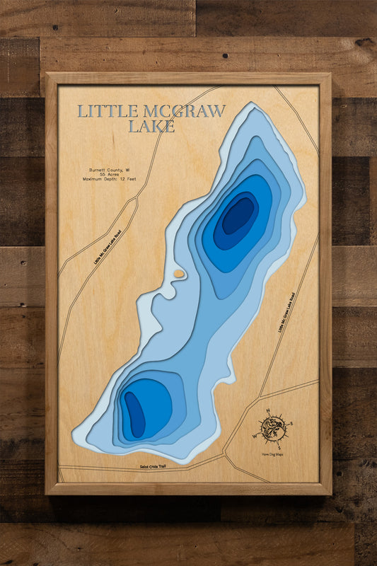 A beautifully detailed, laser-cut, multi-layered wooden map of Little McGraw Lake in Burnett County, Wisconsin, showcasing the intimate 55-acre lake with its natural shoreline detail. The topographic design features a natural wood upper layer and graduated blue water layers illustrating depths from shallow areas to the 12-foot maximum.