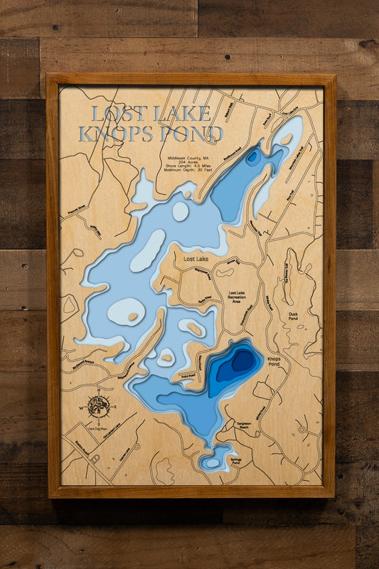 A highly detailed, laser-cut, and multi-layered wooden map of Lost Lake and Knops Pond in Groton, Middlesex County, Massachusetts. The map illustrates the 204-acre reservoir with its distinctive shallow northern Lost Lake basin and the deeper southern Knops Pond section featuring the 30-foot maximum depth, multiple scenic islands, and 4.5 miles of forested shoreline.