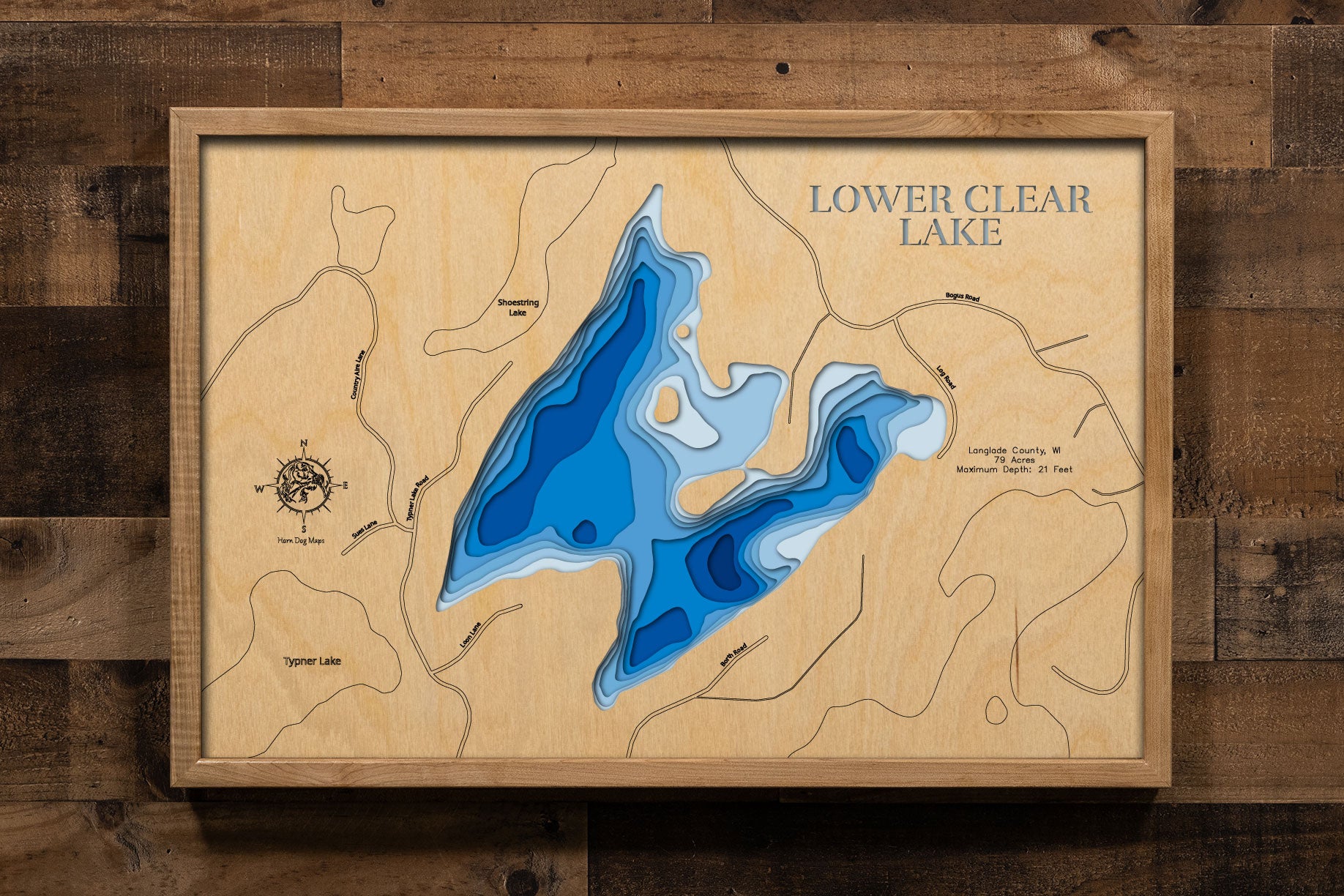 A precision laser-cut, multi-layered wooden map of Lower Clear Lake in Langlade County, Wisconsin — a pristine 79-acre Northwoods lake with award-winning water clarity and no documented invasive species. The natural wood top layer captures its intimate shoreline in fine detail, while a light-to-dark blue gradient conveys its 21-foot depth. A handcrafted statement piece for any Wisconsin lake cabin, home, or outdoor enthusiast's wall.