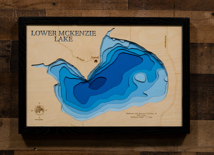 A precision laser-cut, multi-layered wooden map of Lower McKenzie Lake in Washburn and Burnett Counties, Wisconsin, the southernmost lake in the McKenzie chain near Spooner and Trego. The natural wood top layer captures the lake's shoreline in fine detail, while a light-to-dark blue gradient conveys its 17-foot depth. A handcrafted statement piece for any Wisconsin Northwoods cabin, lake home, or outdoor enthusiast's wall.