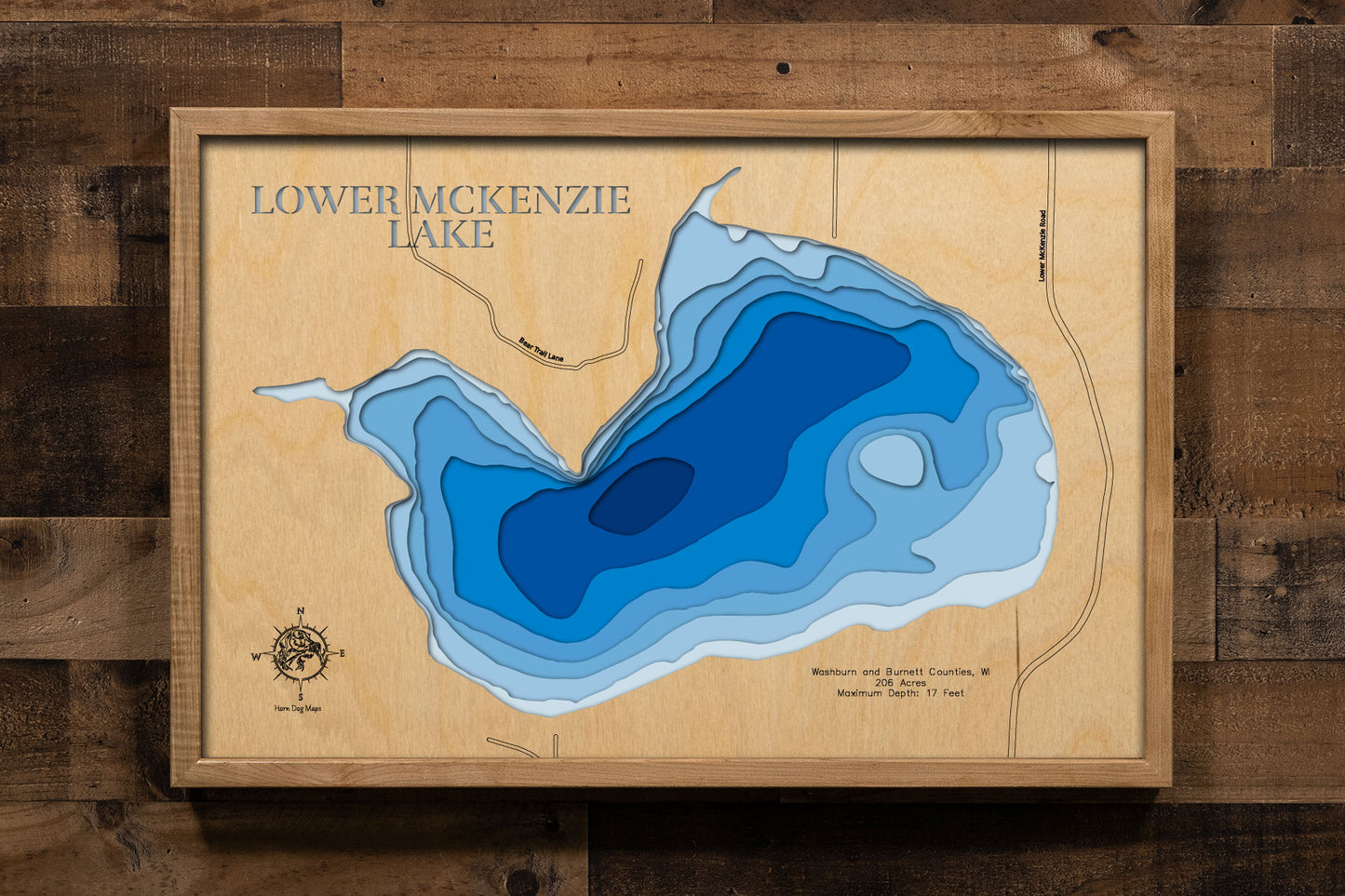 A precision laser-cut, multi-layered wooden map of Lower McKenzie Lake in Washburn and Burnett Counties, Wisconsin, the southernmost lake in the McKenzie chain near Spooner and Trego. The natural wood top layer captures the lake's shoreline in fine detail, while a light-to-dark blue gradient conveys its 17-foot depth. A handcrafted statement piece for any Wisconsin Northwoods cabin, lake home, or outdoor enthusiast's wall.
