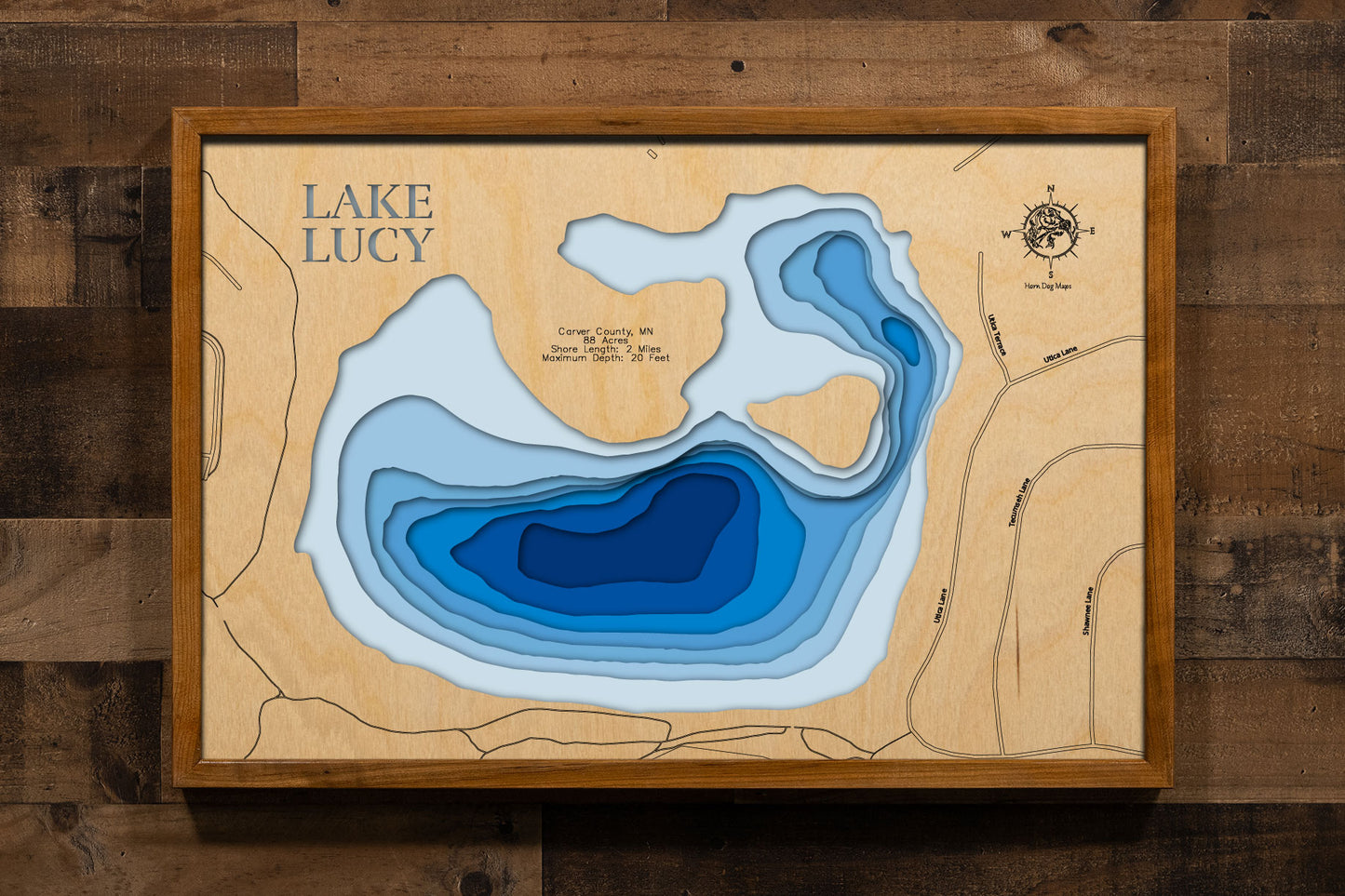 A precision laser-cut, multi-layered wooden map of Lake Lucy in Carver County, Minnesota, a shallow pioneer-named lake in Chanhassen near Lake Minnetonka. The natural wood top layer captures 2 miles of intimate shoreline in fine detail, while a light-to-dark blue gradient conveys the lake's 20-foot depth. A handcrafted statement piece for any Minnesota lake home, cabin, or outdoor enthusiast's wall.