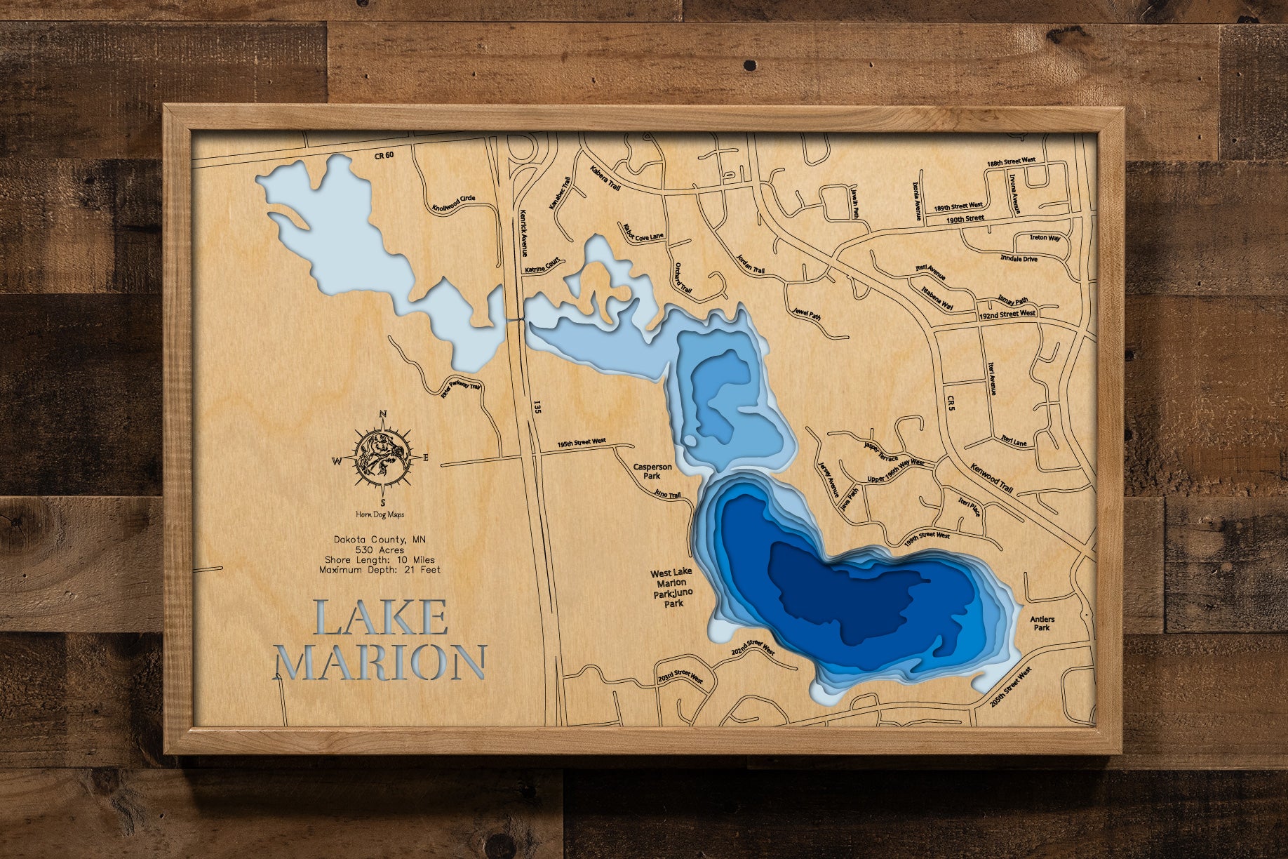 A meticulously crafted, multi-layered laser-cut wooden topographic map of Lake Marion in Dakota County, Minnesota, featuring the three distinct bays across 530 acres, depth contours illustrating the 21-foot maximum depth in the East Bay, the 10 miles of irregular shoreline with numerous small inlets, markers for Antler's Park and Casperson Park with boat launches, the historic Dan Patch Air Rail connection point, and the lake's position within the thriving Lakeville community.