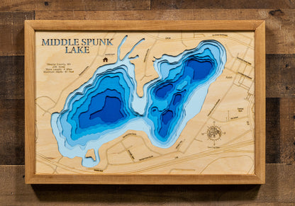 A meticulously detailed, laser-cut, multi-layered wooden topographical map of Middle Spunk Lake in Stearns County, Minnesota, showcasing the 236-acre lake's surface with dramatic depth contours illustrating the transition from vegetated shallows to the impressive 81-foot maximum depth. The natural wood top layer frames four miles of shoreline within the city of Avon, while graduated blue layers create a striking visual depth gradient.