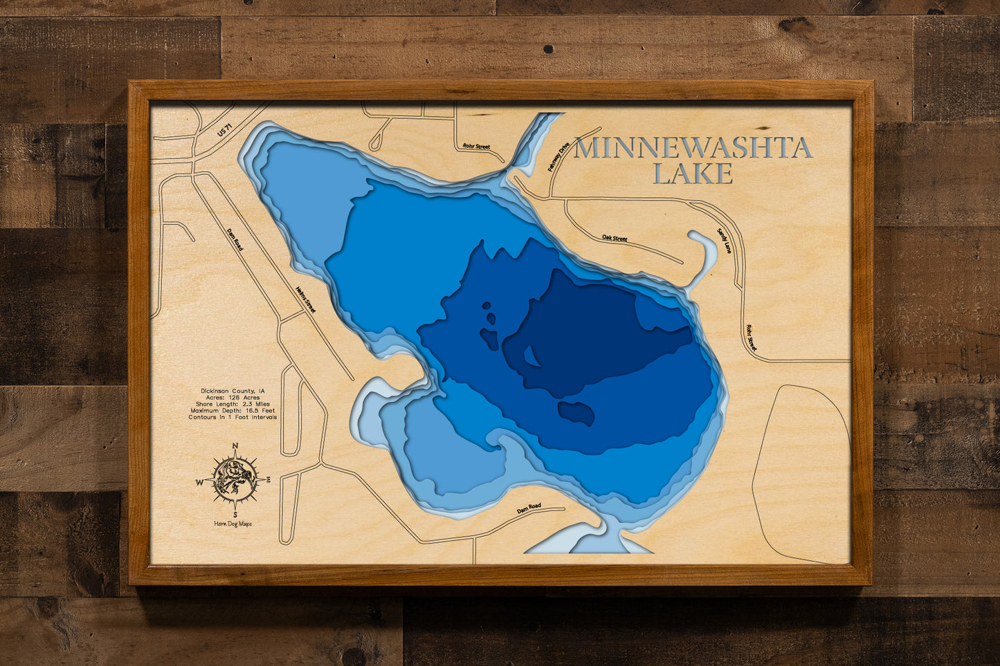 A highly detailed, 3D laser-cut wooden map of Lake Minnewashta in Dickinson County, Iowa. The multi-layered design uses different wood tones to illustrate the lake's bathymetric contours and depths. Etched details include the lake name, county lines, surrounding roads, and nearby towns like Arnolds Park, creating a unique and intricate piece of art.