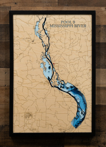 A highly detailed, laser-cut, and multi-layered wooden map of Mississippi River Pool 9, a large impoundment on the border of Iowa, Minnesota, and Wisconsin. The map shows the distinct shape of the river and its extensive 252-mile shoreline, as well as the numerous backwaters. The varying depths of the river pool, reaching a maximum of 15 feet, are represented by different layers of wood.