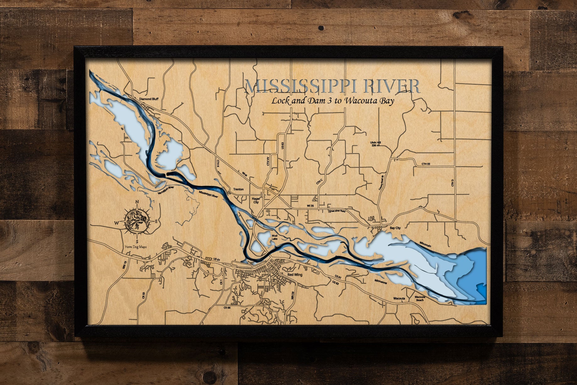 A laser-cut, layered wooden map showcasing a detailed section of the Mississippi River from Lock and Dam 3 to Wacouta Bay. The map highlights the river's main channel, numerous backwaters, and islands, all set within the dramatic bluffs of the Minnesota and Wisconsin shorelines. The location of the Lock and Dam 3 is clearly visible, as are the communities of Red Wing, MN, and Hager City, WI. The varying depths of the river are represented by different layers of wood, illustrating its impressive underwater t