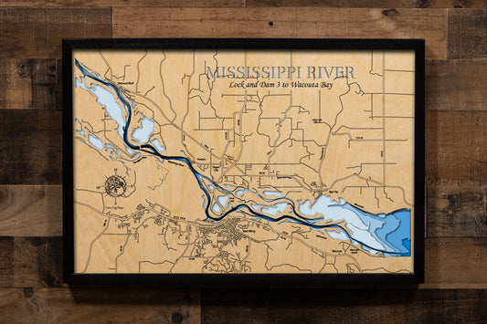 A laser-cut, layered wooden map showcasing a detailed section of the Mississippi River from Lock and Dam 3 to Wacouta Bay. The map highlights the river's main channel, numerous backwaters, and islands, all set within the dramatic bluffs of the Minnesota and Wisconsin shorelines. The location of the Lock and Dam 3 is clearly visible, as are the communities of Red Wing, MN, and Hager City, WI. The varying depths of the river are represented by different layers of wood, illustrating its impressive underwater t