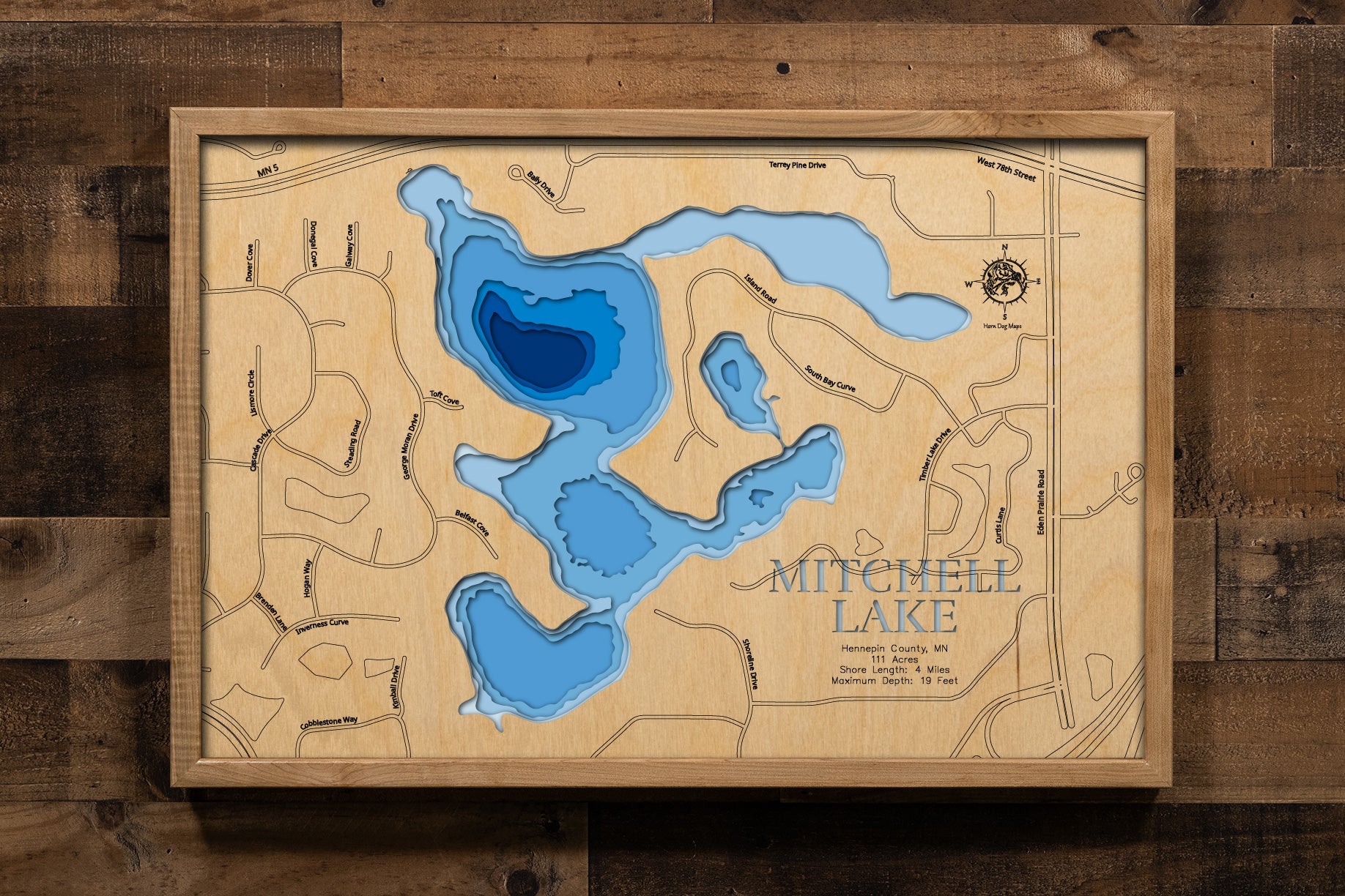 A precision laser-cut, multi-layered wooden map of Mitchell Lake in Hennepin County, Minnesota, near Eden Prairie and Chanhassen. The natural wood top layer captures 4 miles of lily pad-lined shoreline in fine detail, while a light-to-dark blue gradient highlights the lake's 19-foot depth. A handcrafted statement piece for any Twin Cities lake home, cabin, or outdoor enthusiast's wall.