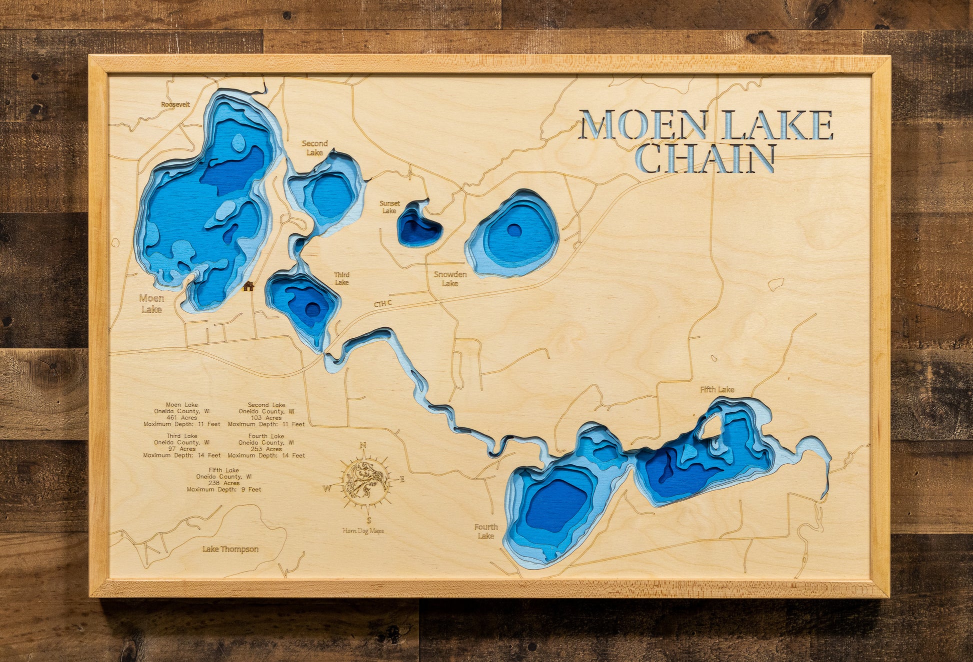 A highly detailed, laser-cut, and multi-layered wooden map of the Moen Lake Chain in Oneida County, Wisconsin. The map showcases all five interconnected lakes—Moen, Second, Third, Fourth, and Fifth—linked by the Pelican River, with depth contours highlighting the varying shallow depths from 9 to 14 feet across the 1,100-acre chain system.