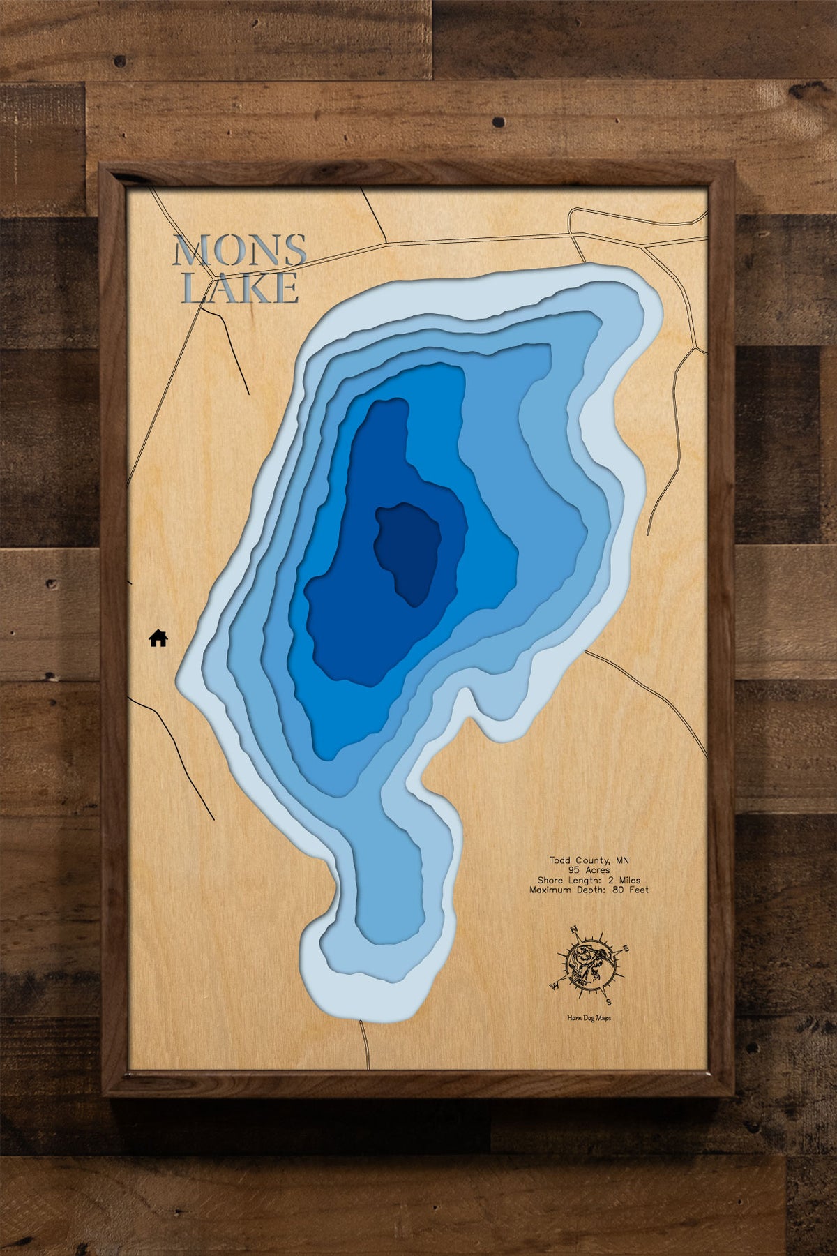 A precision laser-cut, multi-layered wooden map of Mons Lake in Todd County, Minnesota, a 95-acre lake near Long Prairie with a striking maximum depth of 80 feet. The natural wood top layer captures 2 miles of shoreline in fine detail, while a light-to-dark blue gradient beautifully conveys the lake's remarkable depth. A handcrafted statement piece for any Minnesota lake cabin, home, or outdoor enthusiast's wall.