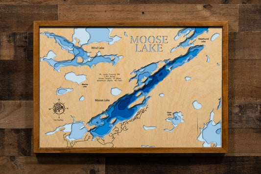 A magnificently detailed, laser-cut, multi-layered wooden topographical map of Moose Lake in Lake County, Minnesota, showcasing the pristine 1,301-acre wilderness lake within the Boundary Waters Canoe Area Wilderness with depth contours from rocky shallows to the 40-foot maximum depth. The natural wood top layer frames approximately 10 miles of entirely undeveloped shoreline, five designated campsites, portage trails to Newfound and Sucker Lakes, and BWCA Entry Point 25 access, while graduated blue lay