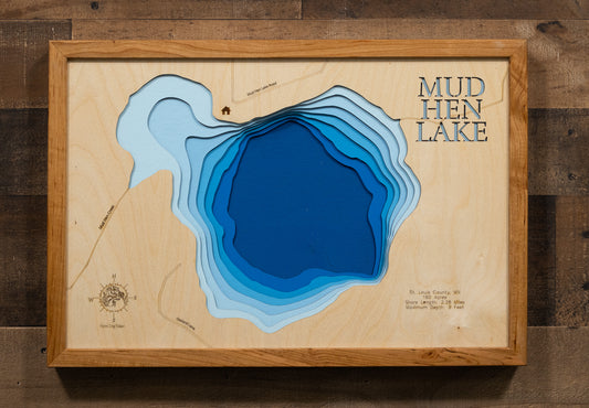 A laser-cut, layered wooden map of Mud Hen Lake in St. Louis County, Minnesota. The distinct shape of this natural lake, with its 2.28-mile shoreline, is clearly visible within the forested landscape of northeastern Minnesota near Makinen. The varying depths of the lake, reaching a maximum of 9 feet, are represented by different layers of wood, illustrating its shallow underwater topography.