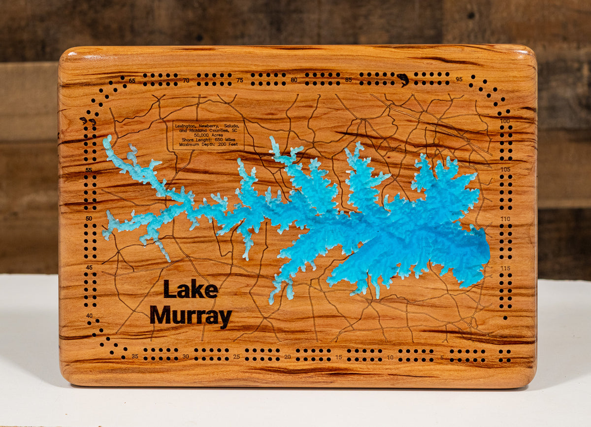 A square wooden cribbage board game featuring a laser-engraved map of Lake Murray, with a bright blue lake silhouette and black text reading 'Lake Murray.' The board has a warm honey-toned wood grain finish and circular peg holes around the edges.