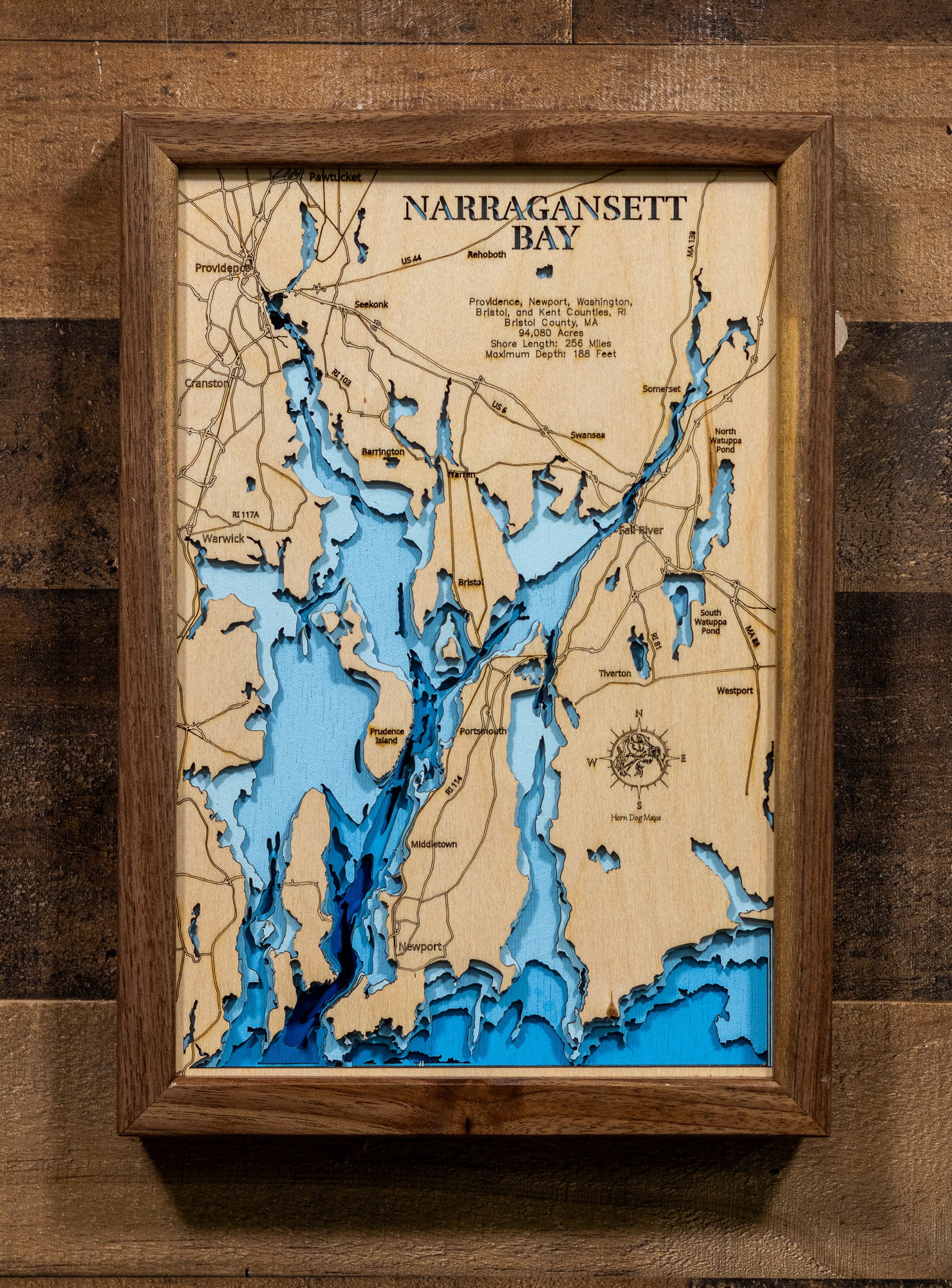 An expertly crafted laser-cut wooden map of Narragansett Bay, New England's largest estuary, showcasing the 147-square-mile bay spanning Rhode Island and Massachusetts, over 30 islands including Aquidneck, Conanicut, and Prudence, 256 miles of intricate shoreline, three distinct passages (West, East, and Sakonnet River), and layered depth contours revealing the 188-foot maximum depth.